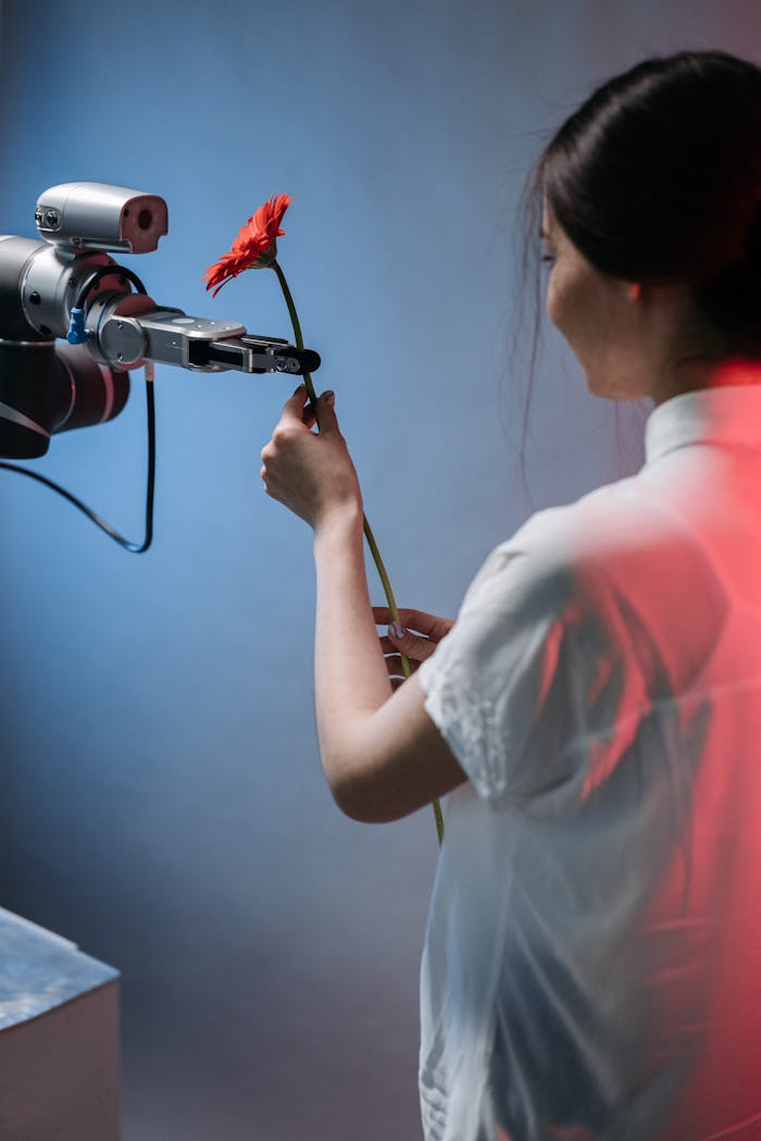 brand-01 A robotic arm delicately holds a red flower as a woman interacts with it.